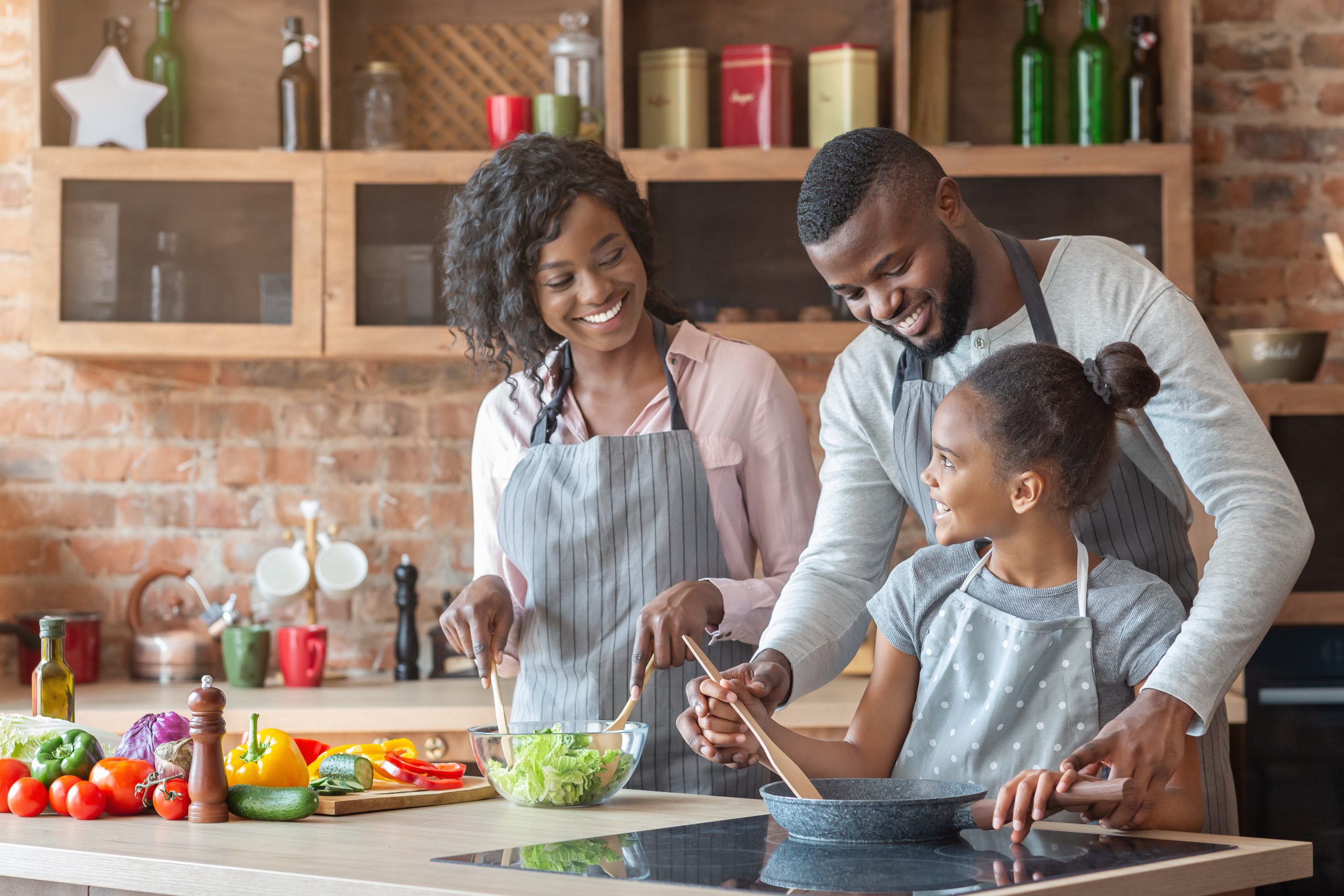 Kind black parents teaching their adorable daughter how to cook healthy food, kitchen interior, copy space